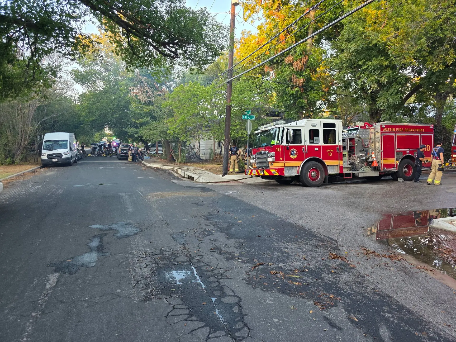 Fire engine and firefighters on a tree-lined residential street after a house fire, water and fire damage restoration