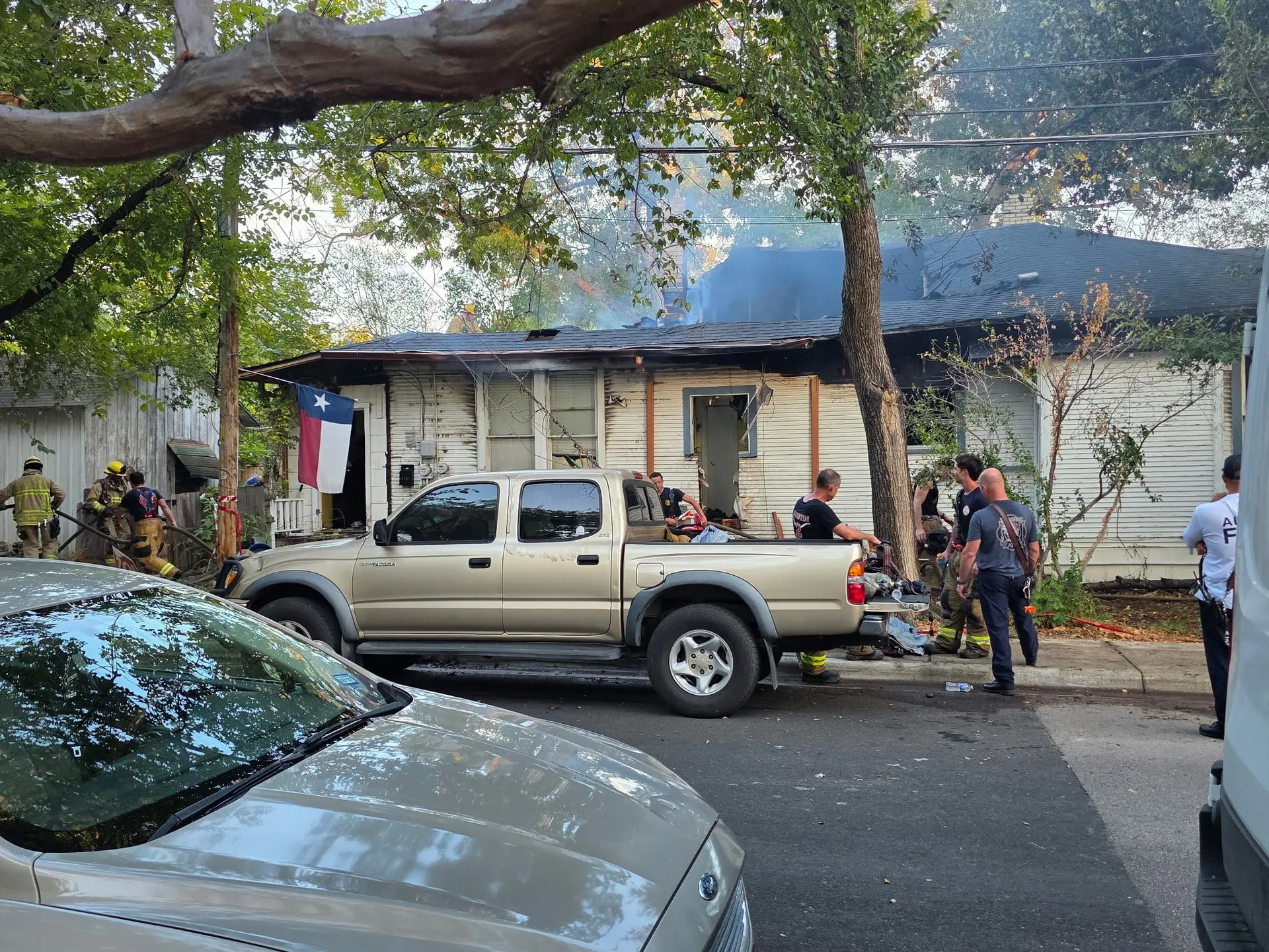Firefighters outside a one-story house with smoke still rising from the roof, water and fire damage restoration