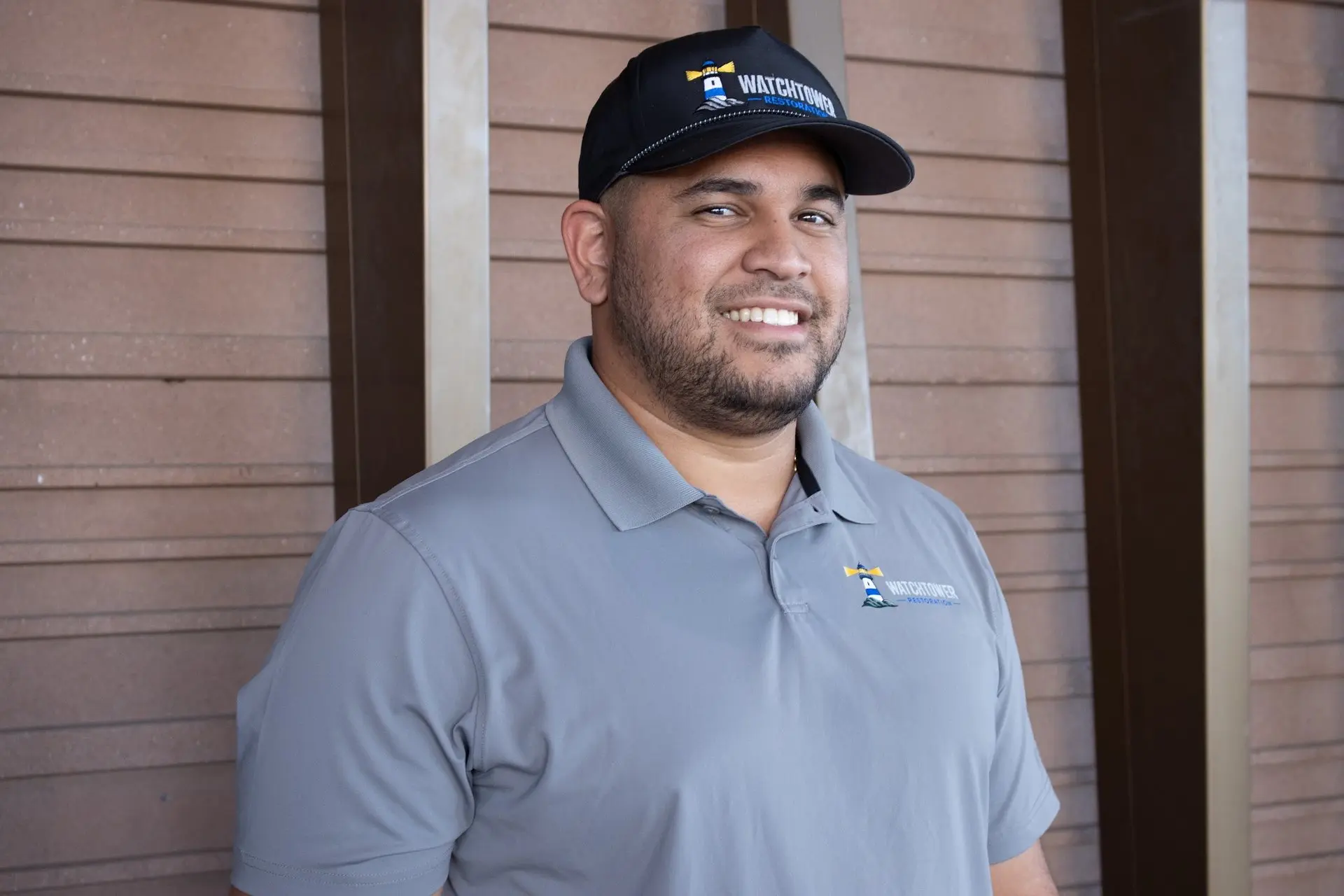 Smiling team member in a grey polo shirt and black cap, water and fire damage restoration